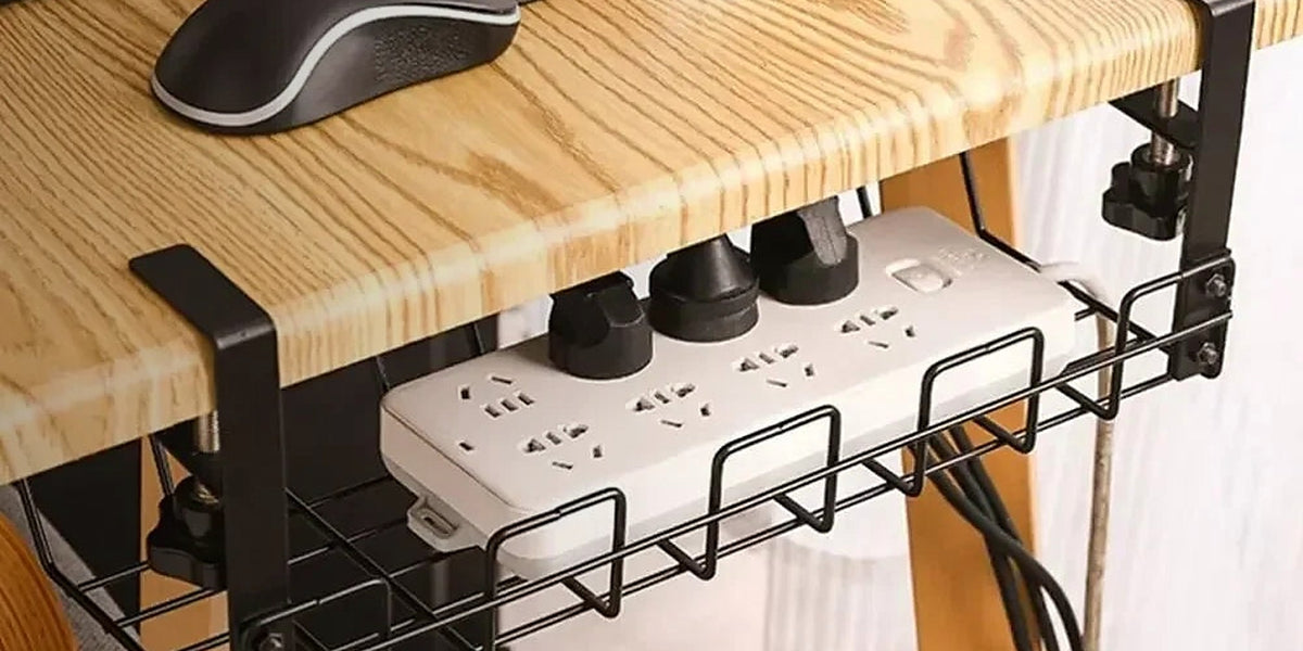 A clamp-on wire tray under a wood desk holding a power strip with cables routed away