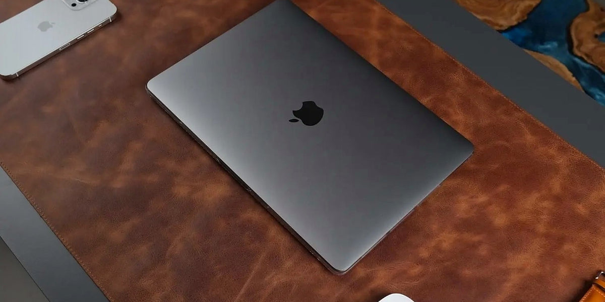 A full-grain leather desk pad covering a desk, with a laptop, mouse and phone on it
