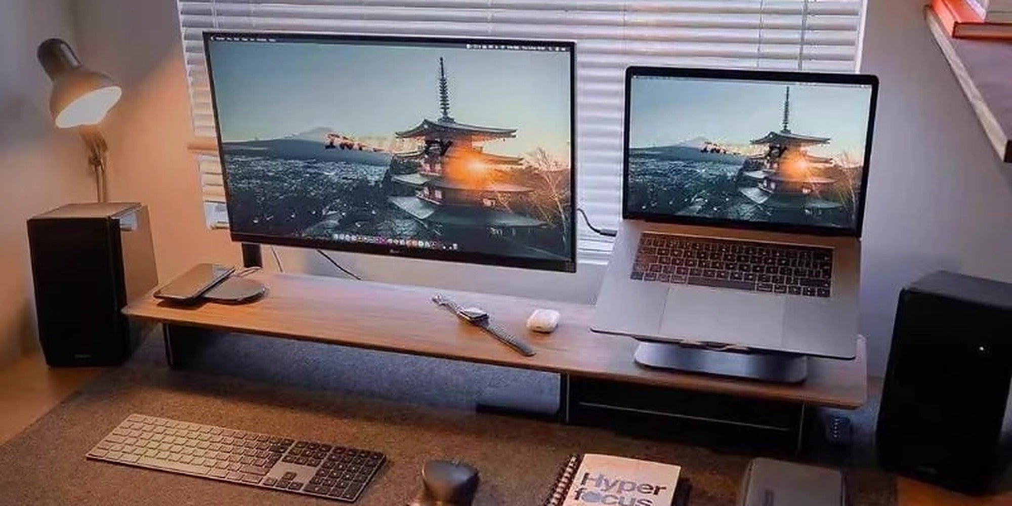 A long walnut monitor riser lifting a monitor and laptop above a desk mat and keyboard