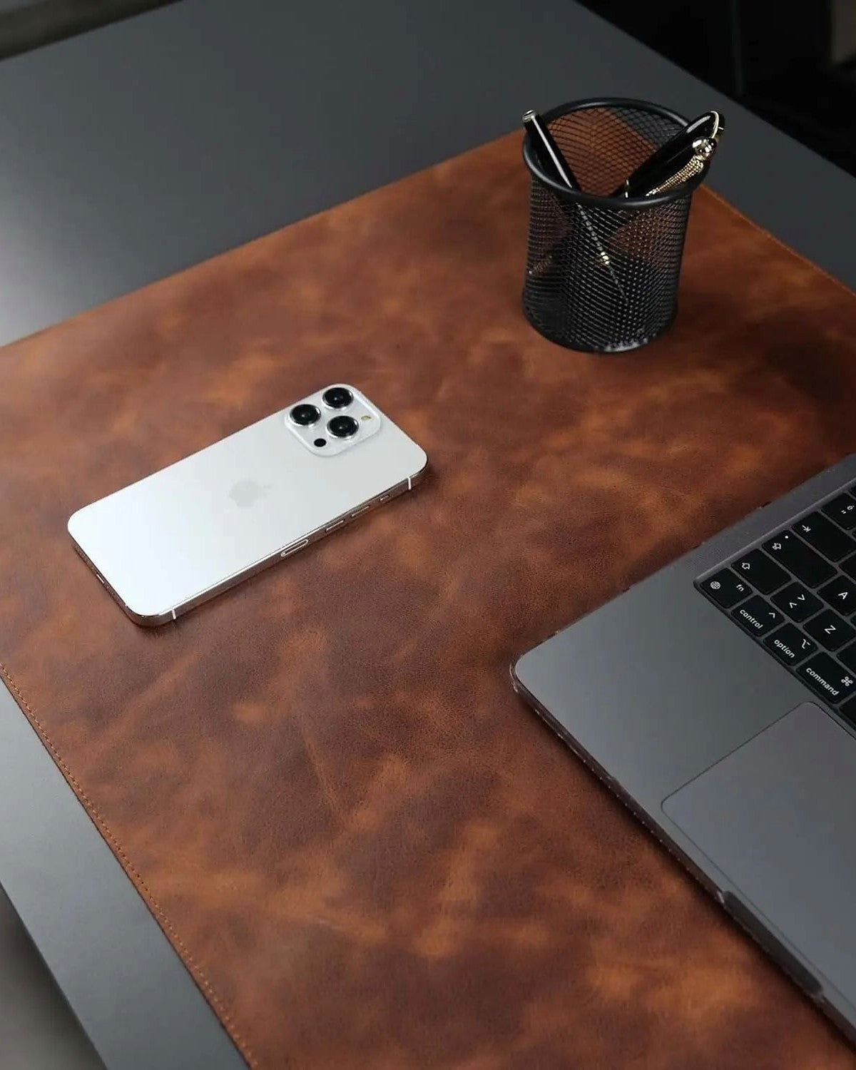 A full-grain leather desk pad with a phone, pen cup and laptop on it